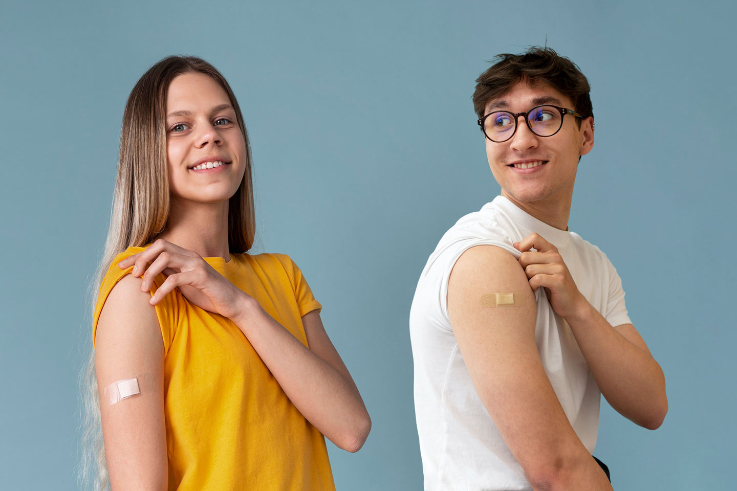 Ein Mädchen und ein Junge zeigen ihre Pflaster am Oberarm nach einer HPV-Impfung